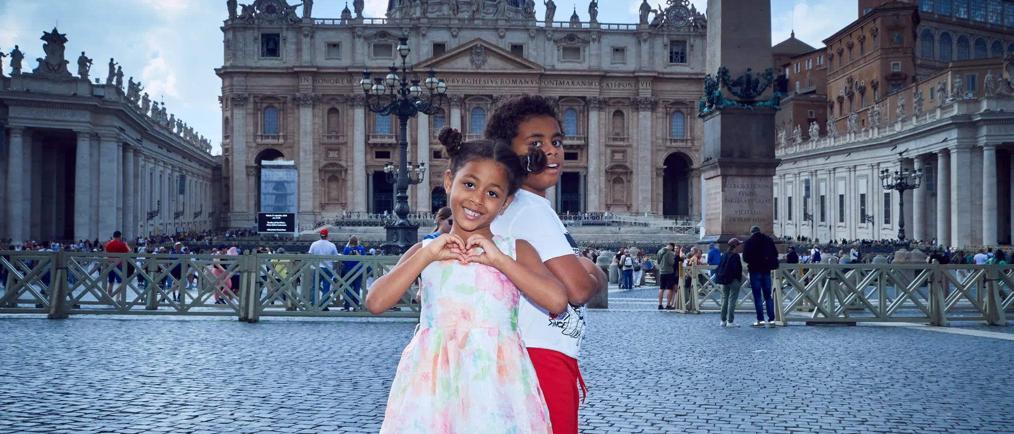 Smiling child making heart gesture on St Peter’s Square in Vatican City, Rome