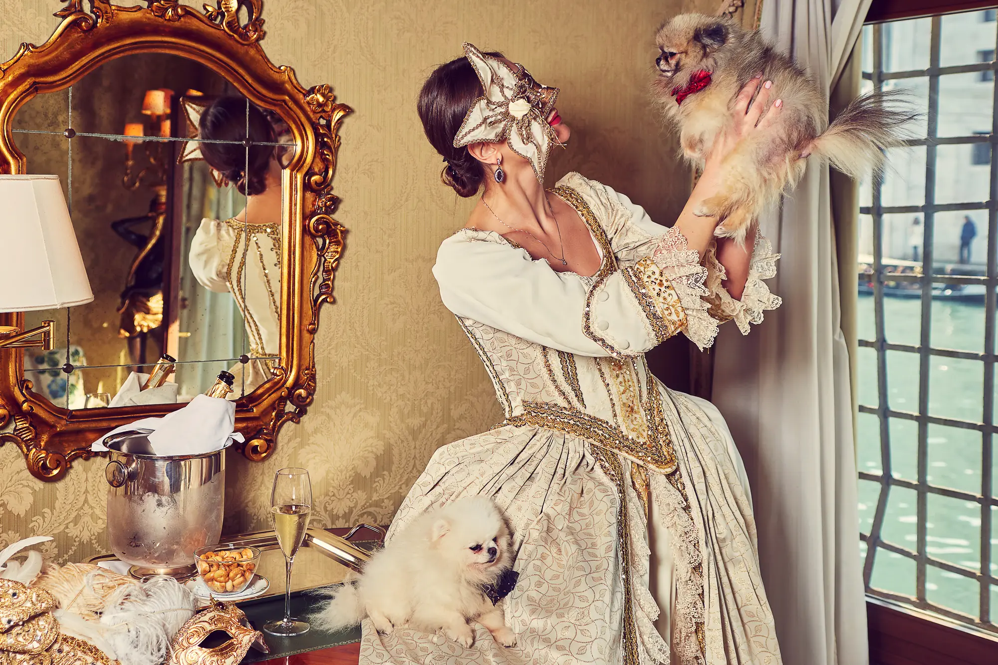 Photographer in Venice shooting woman in Venetian carnival dress with two Pomeranian dogs in luxury hotel room