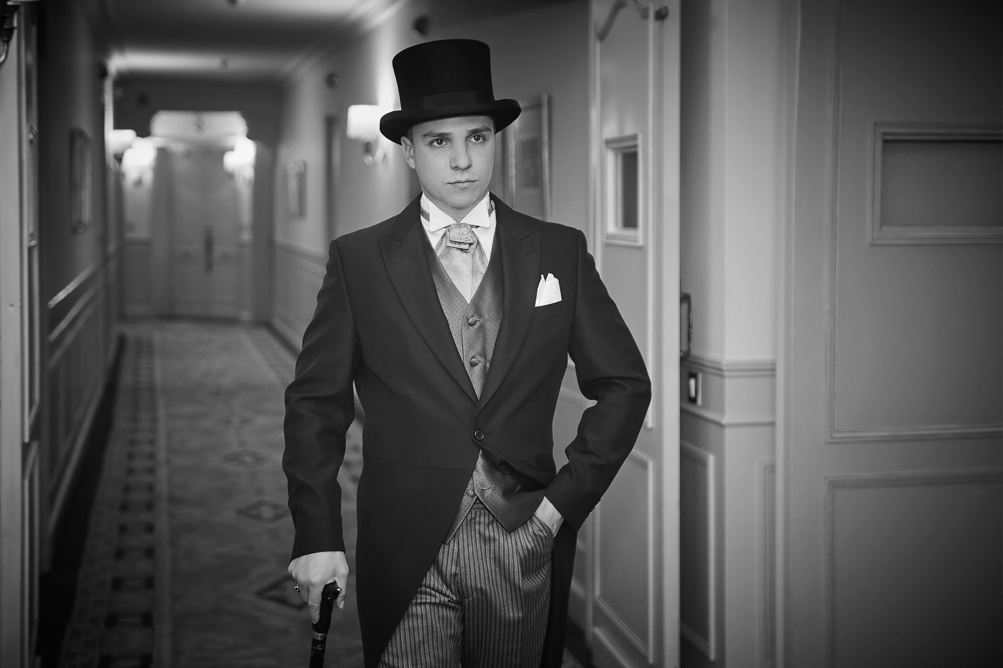 Pavel Manylov in a tailcoat and top hat standing in a luxurious historic hotel corridor