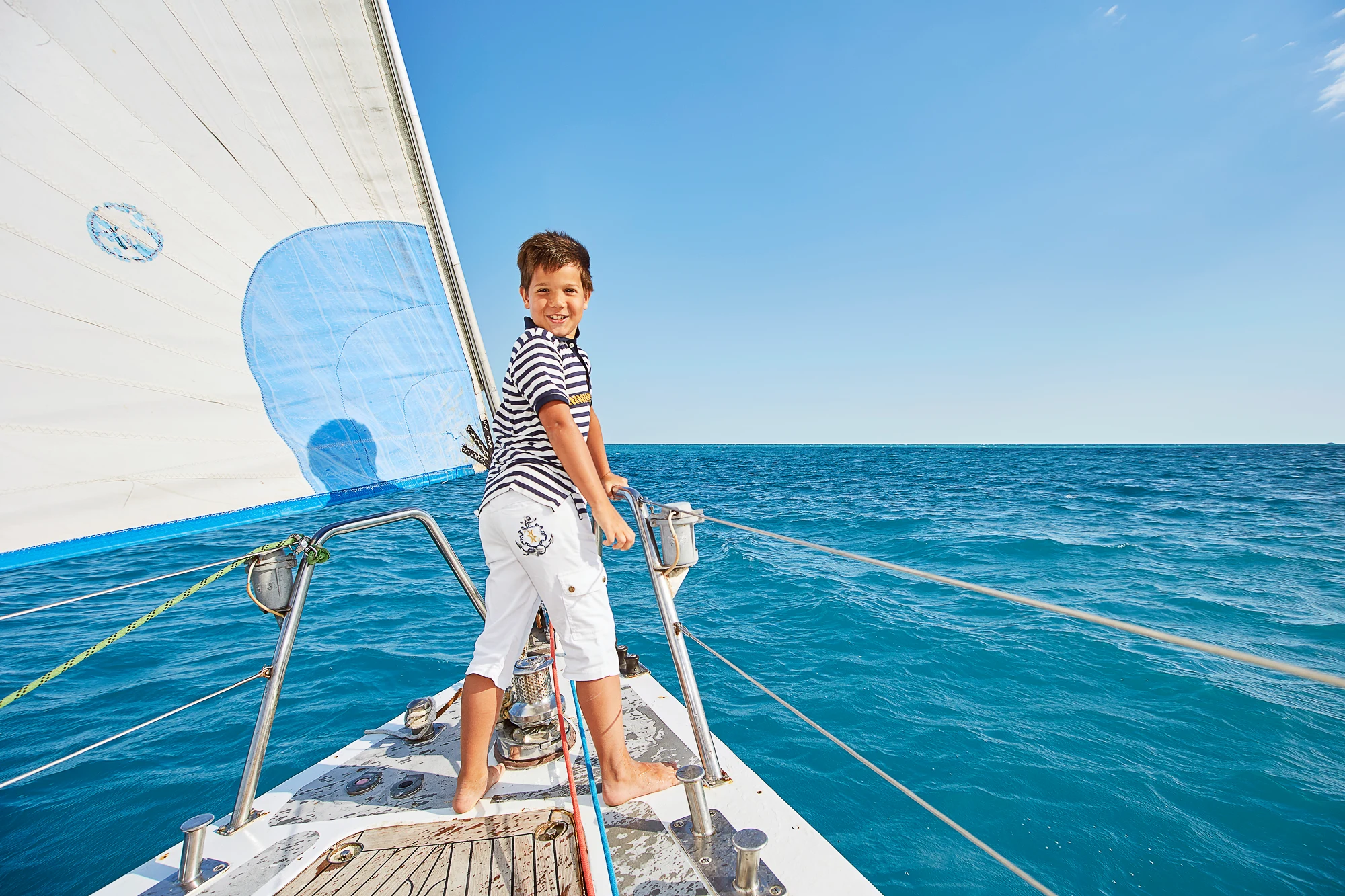 Smiling boy standing on the bow of a sailing yacht on a sunny day at sea in Italy