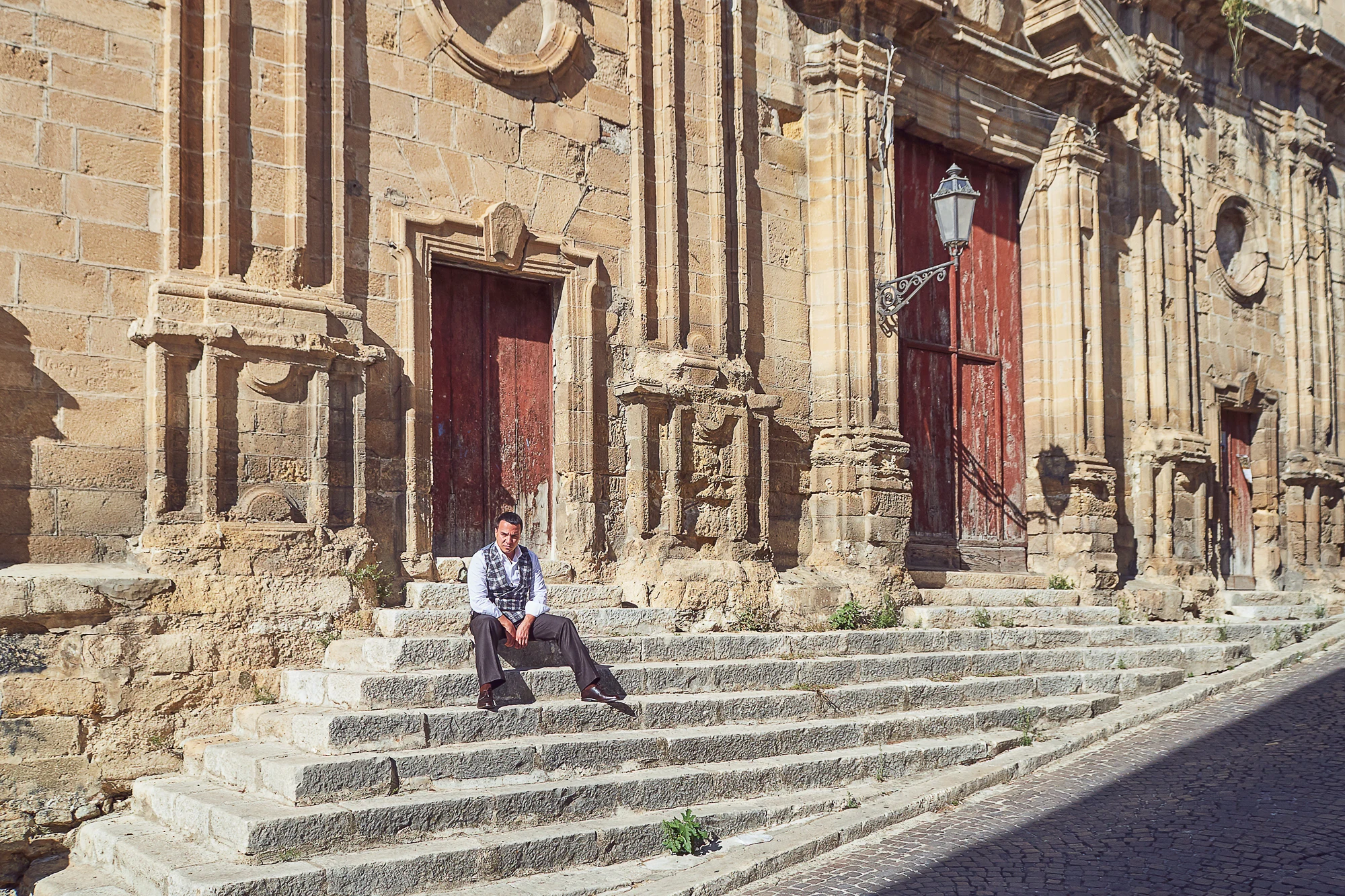 Man in a vest sitting on stone steps of an old church in Corleone, Sicily. (Pavel Manylov)
