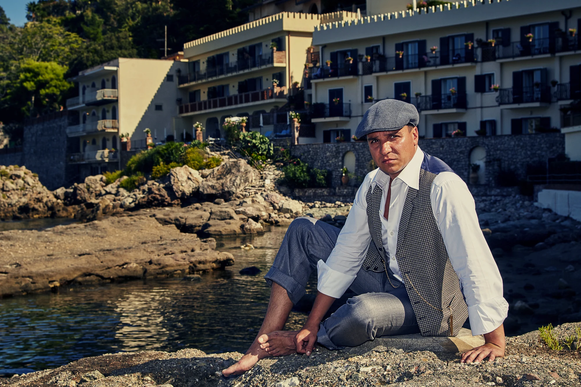 Man in vintage outfit sitting on rocks by Italian seaside hotel (Pavel Manylov)