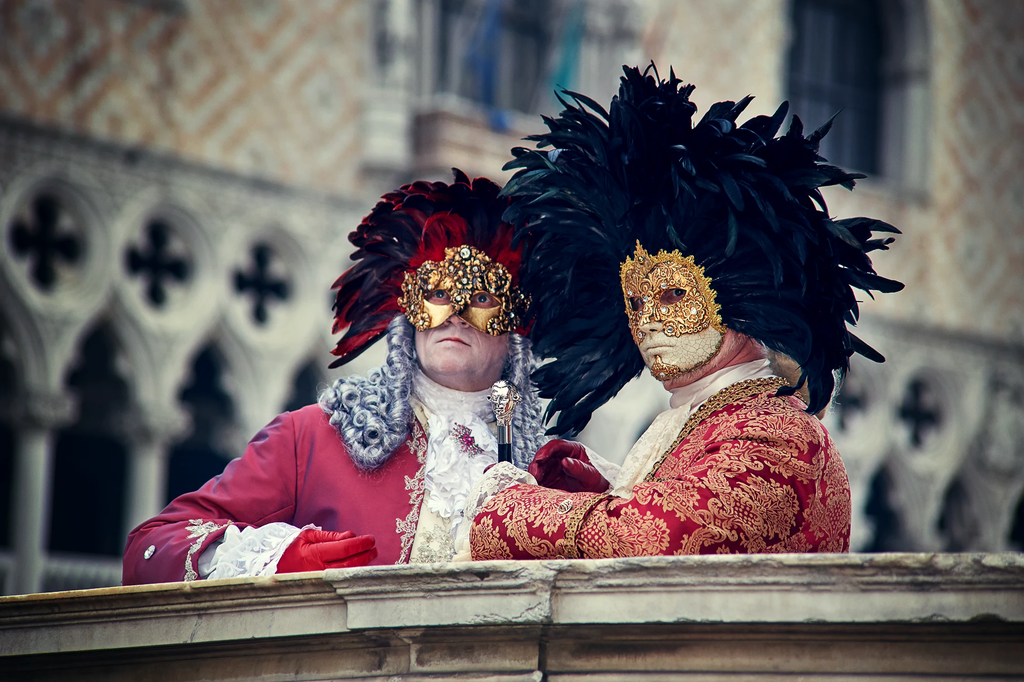 Two people in elaborate Venetian carnival masks and costumes near historic architecture