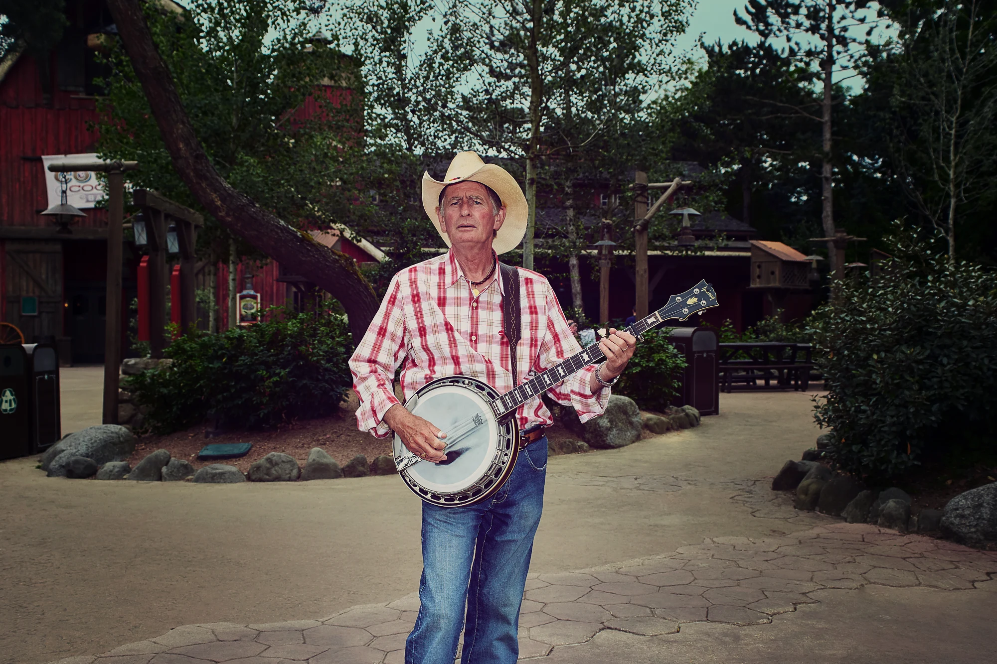 Western style portrait of an older man in cowboy hat playing banjo outdoors