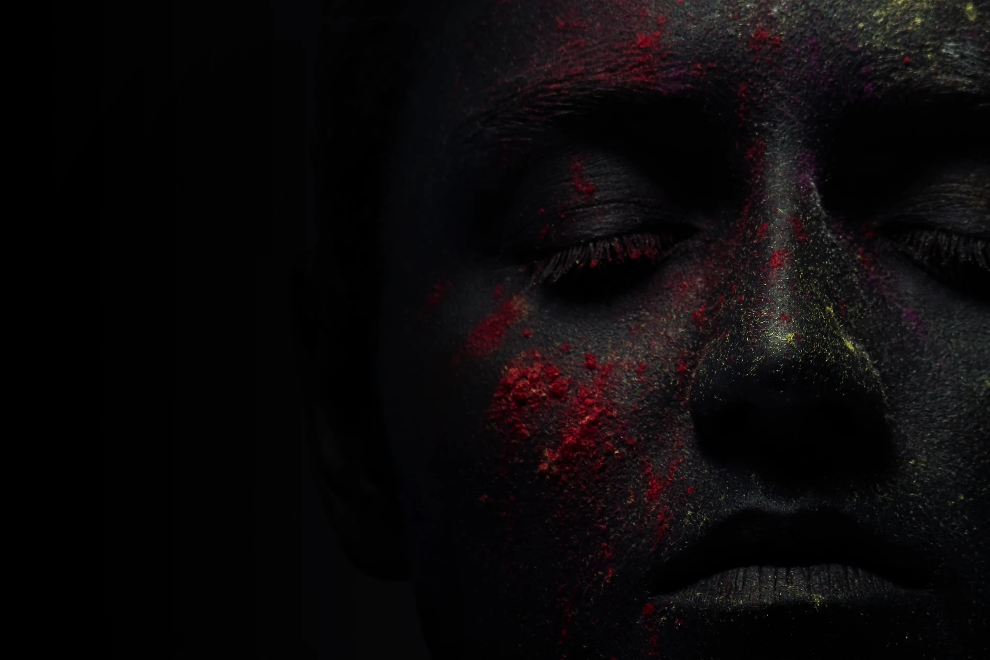 Closeup of woman with black painted face and colorful powder pigments on skin with eyes closed