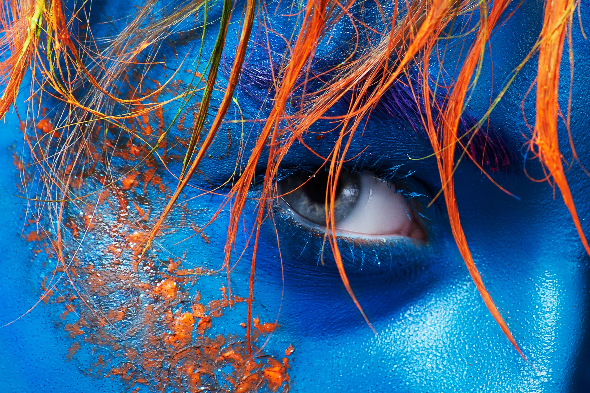 Closeup of human eye with bright blue face paint and orange hair strands
