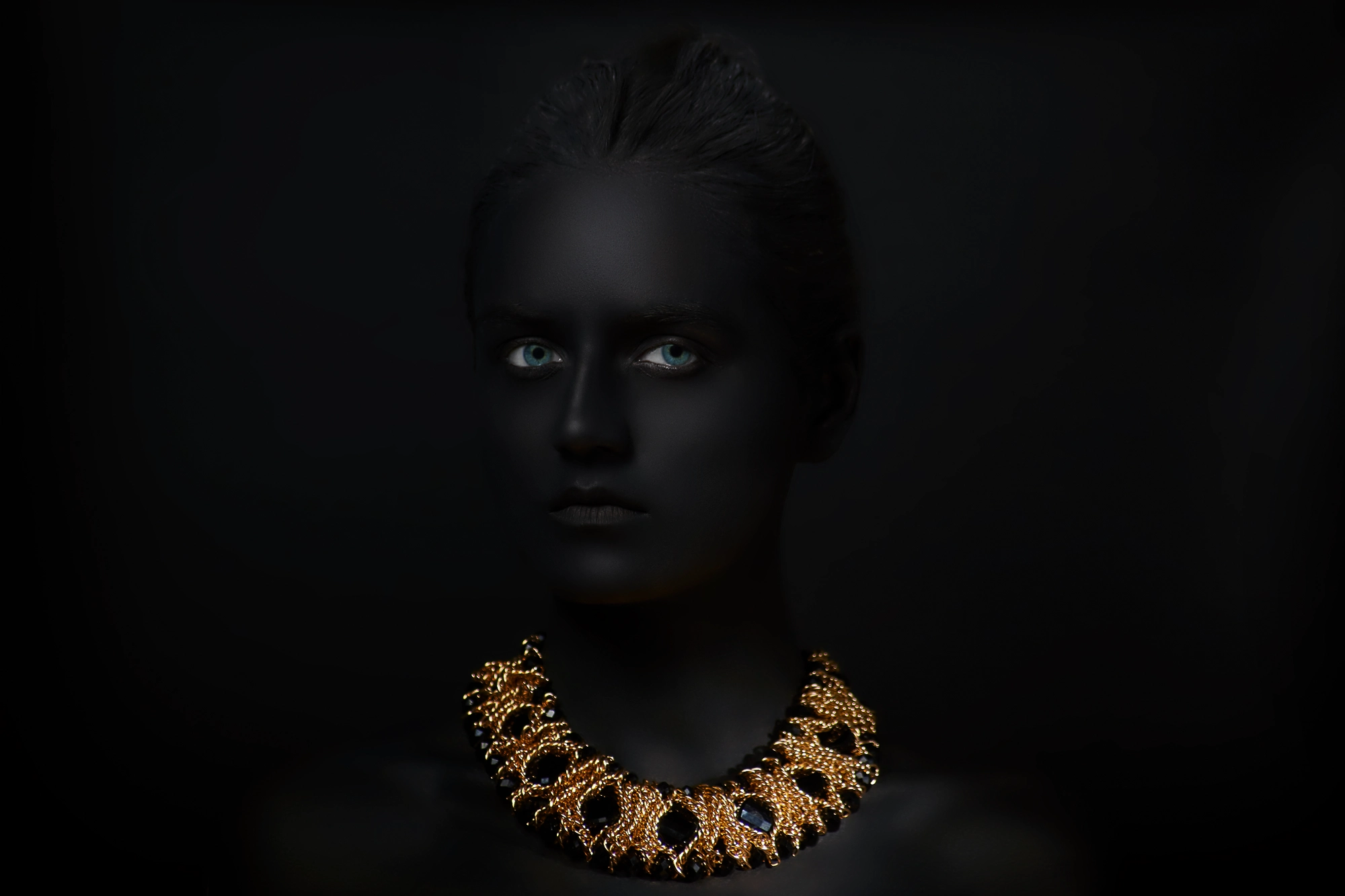 Dramatic studio portrait with black body paint and a bright golden statement necklace in the dark