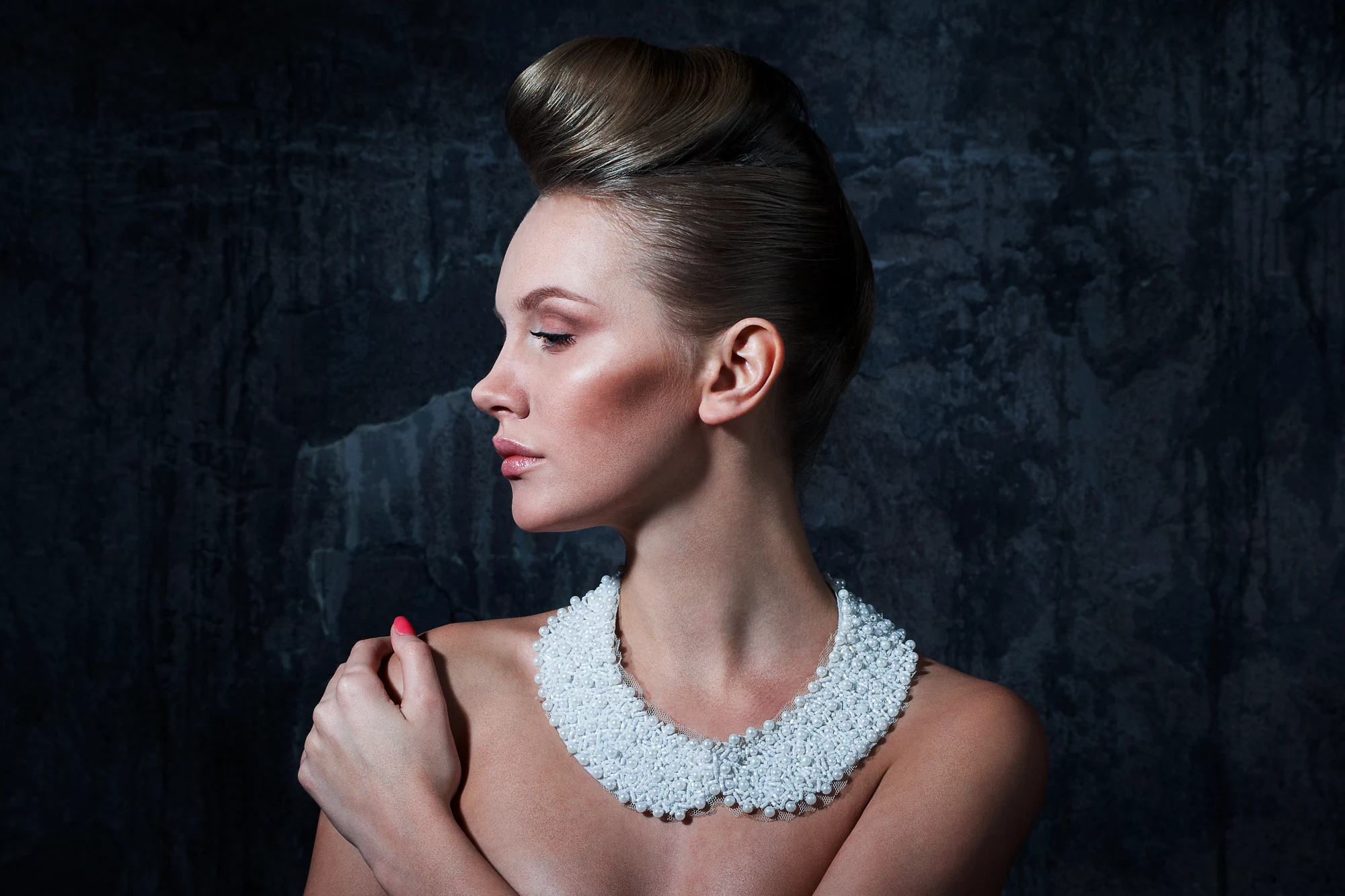 Side profile studio portrait of an elegant woman wearing a white beaded collar on dark background