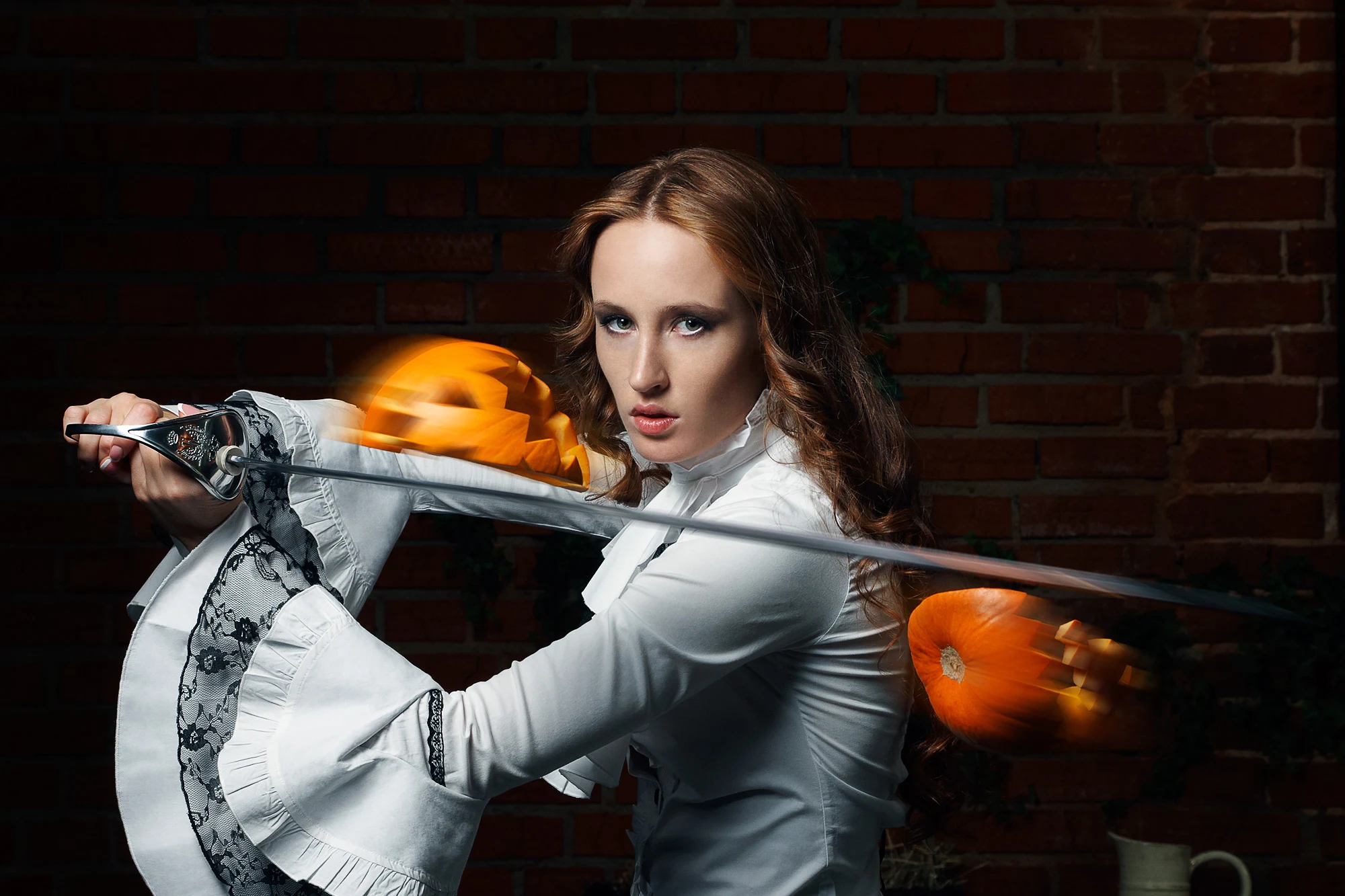 Woman in white blouse swinging sword through flying Halloween pumpkins in studio