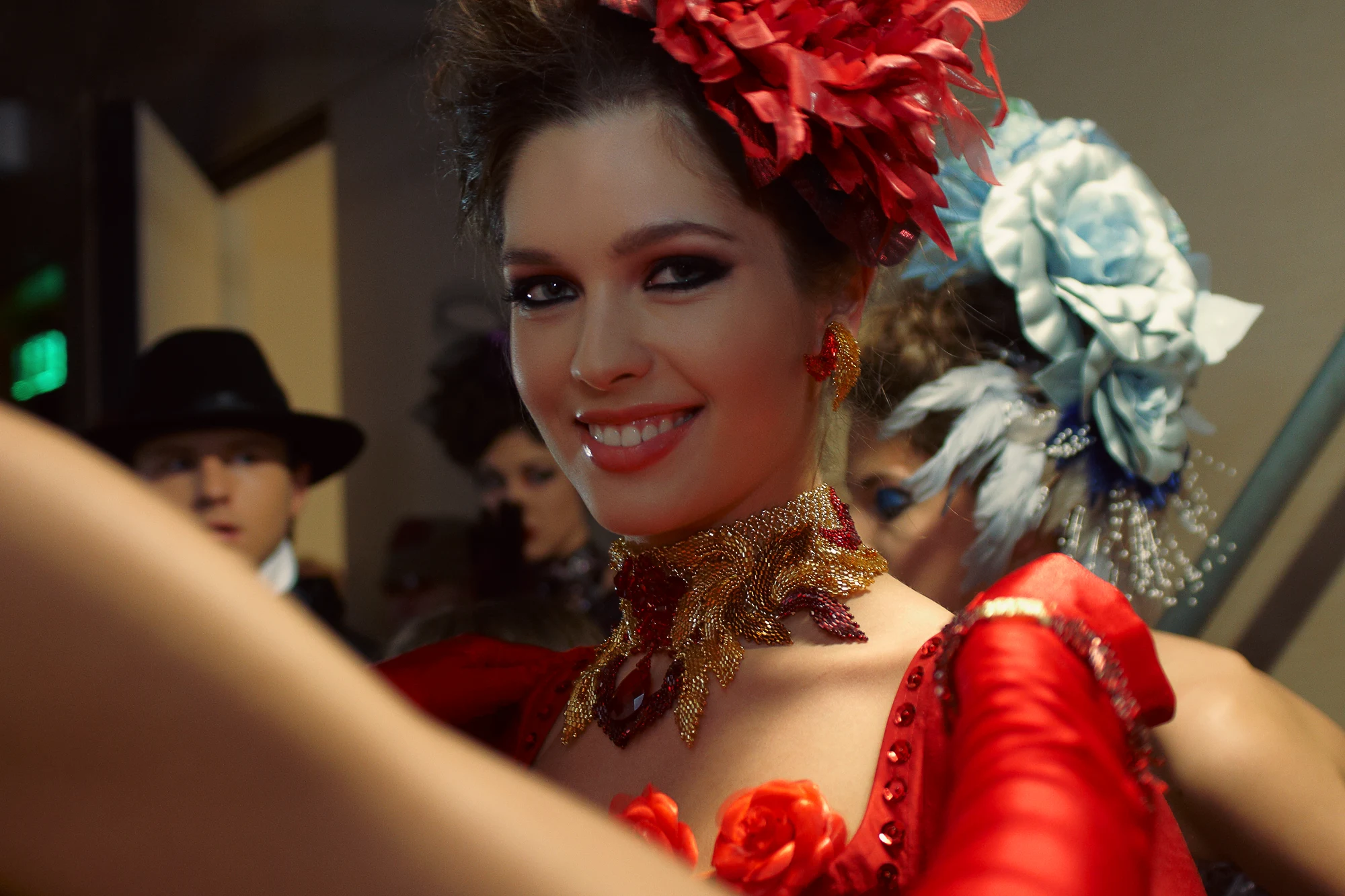 Backstage fashion photographer capturing smiling model in red costume with statement jewelry before performance