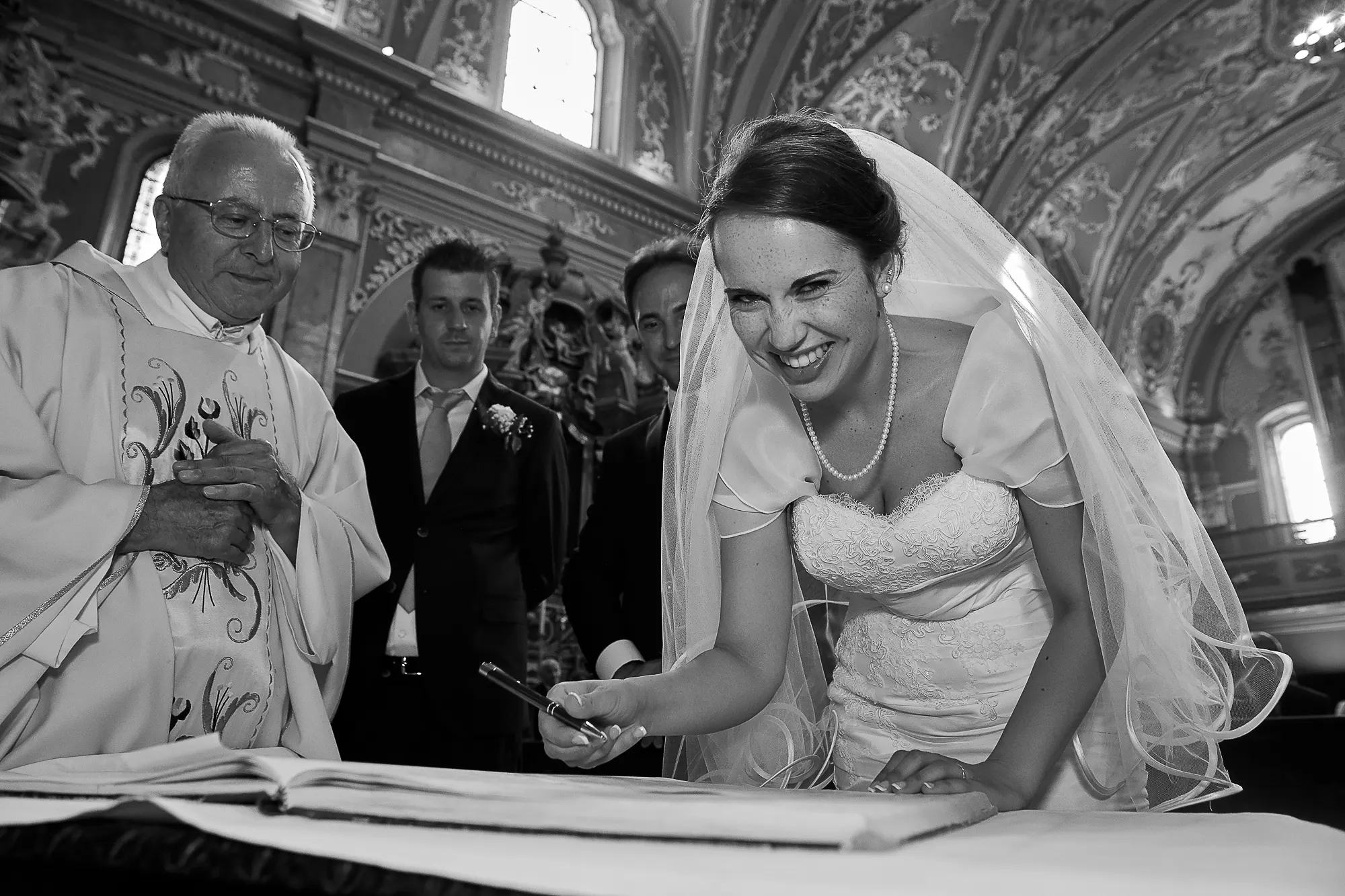 Smiling bride signing the church marriage register beside the priest and witnesses during a wedding ceremony in Italy