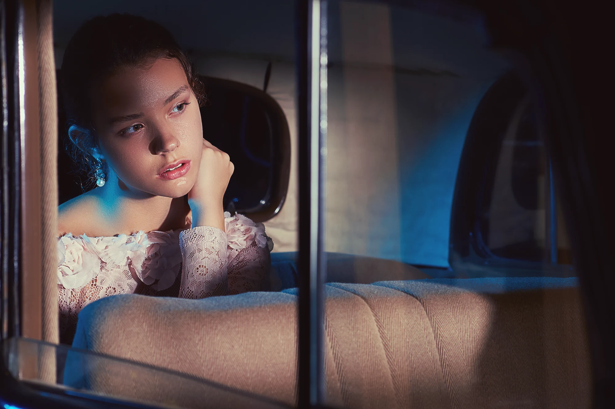 Artistic bridal portrait of young woman in lace dress sitting in vintage car at night