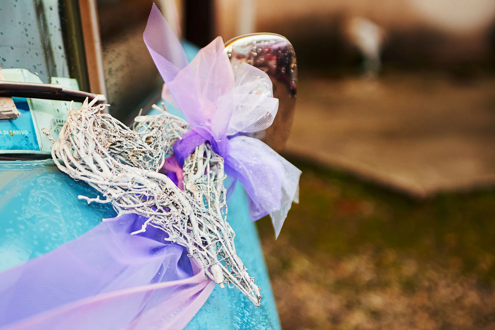 Close up of rustic heart shaped wedding car decoration with purple ribbon and tulle on blue vintage car