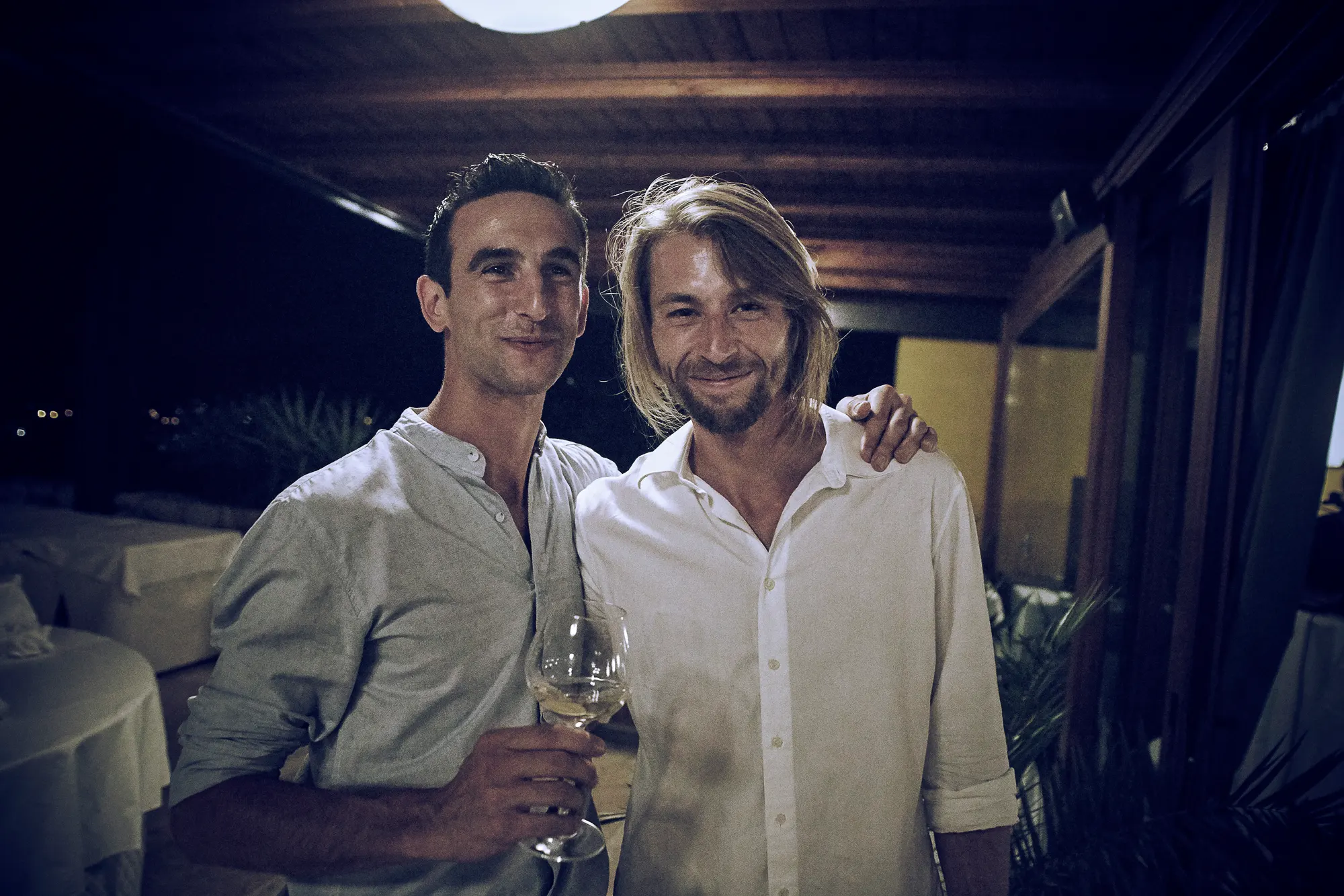 Two friends at evening event in Italy smiling and posing with a glass of white wine