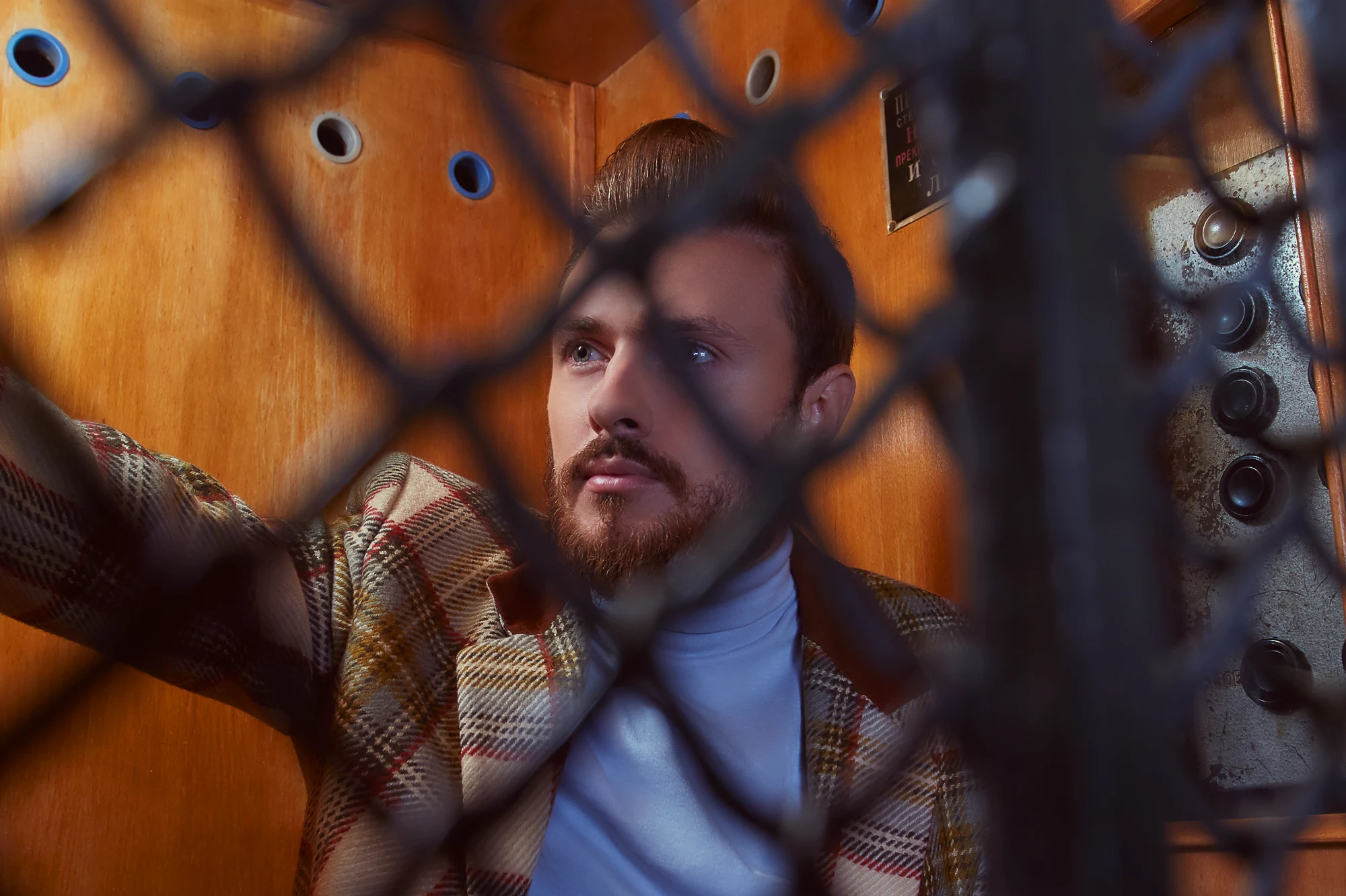 Groom in checked jacket posing inside old vintage elevator in retro cinematic style