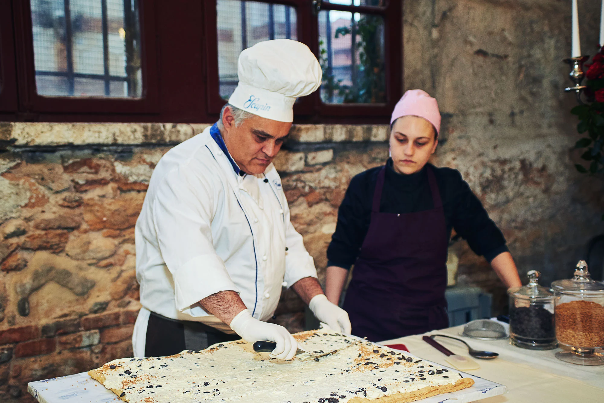 Italian chef in a tall hat cutting a large dessert in the kitchen during a wedding reception