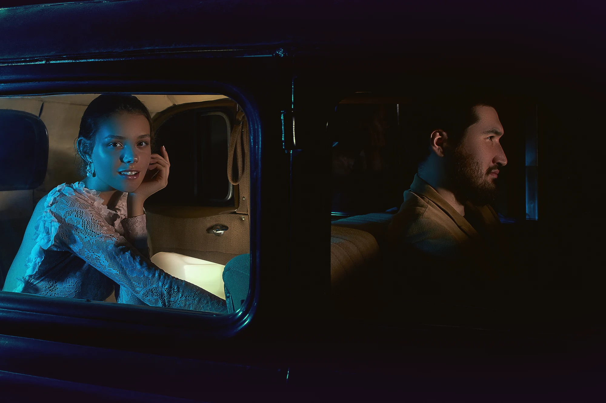 Romantic couple sitting inside a vintage car at night with dramatic blue cinematic lighting