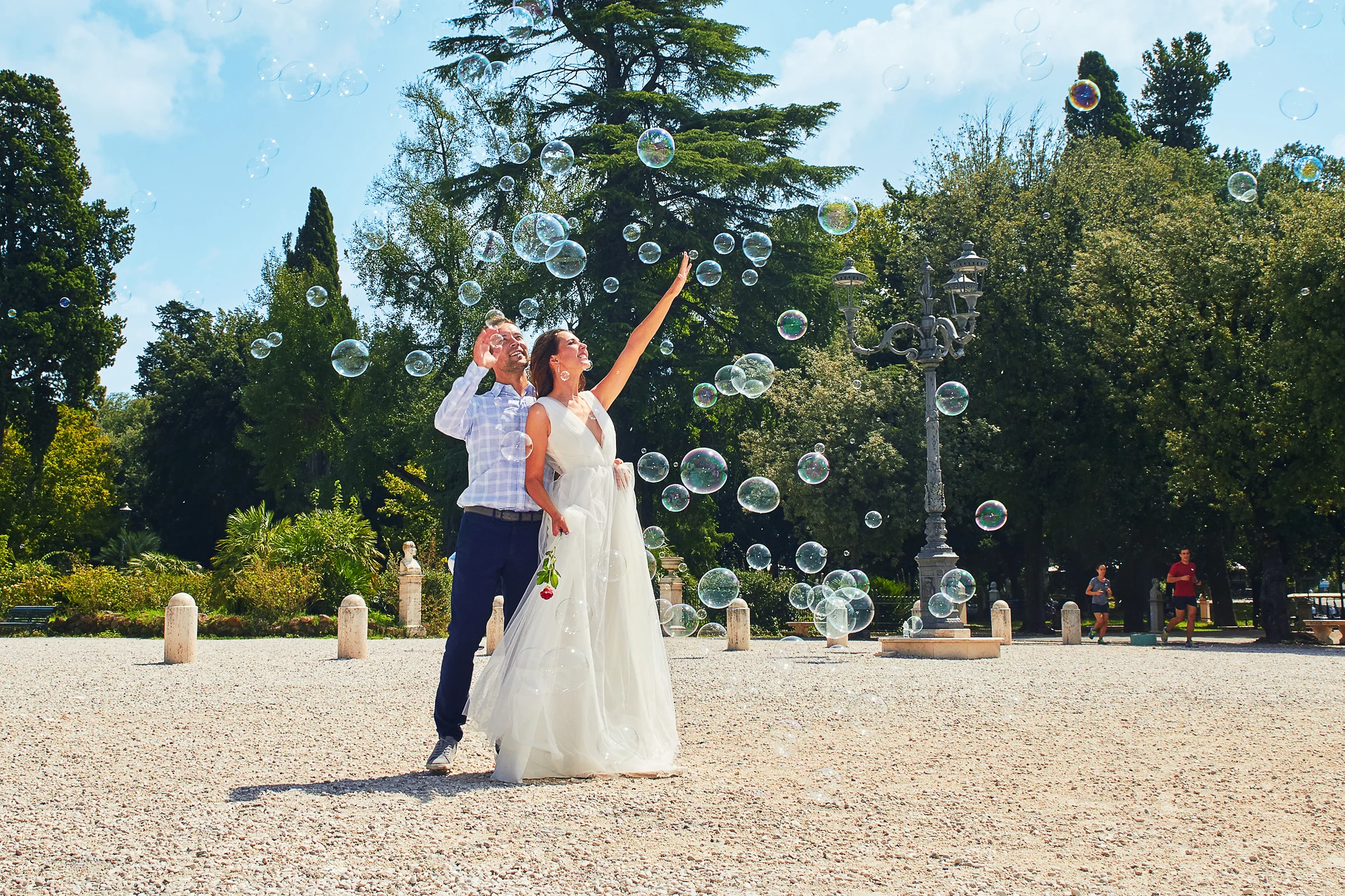 Happy wedding couple playing with soap bubbles in sunny park, wedding photographer in Rome Italy