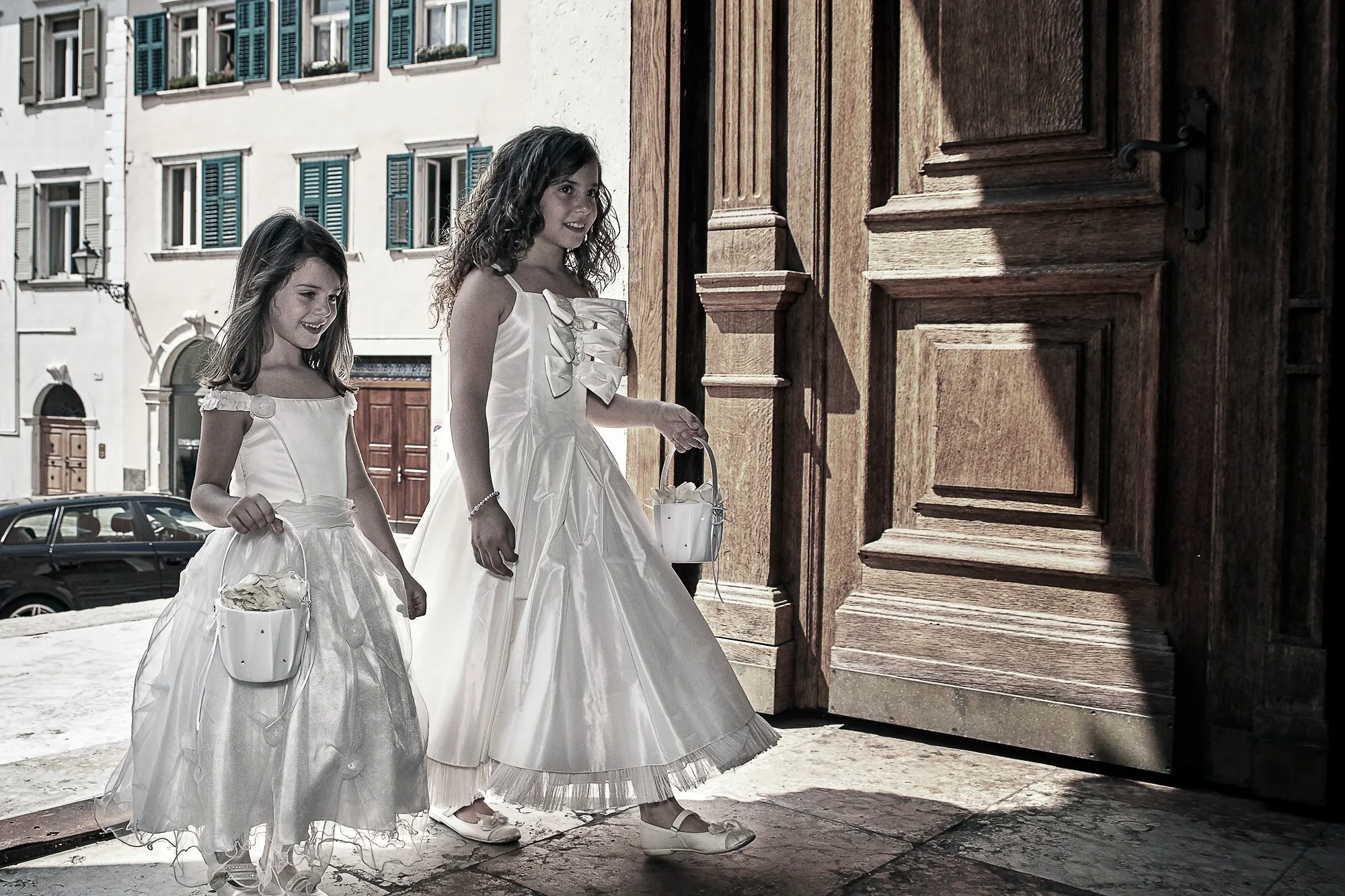 Wedding photographer in Italy capturing two flower girls entering old church with flower baskets
