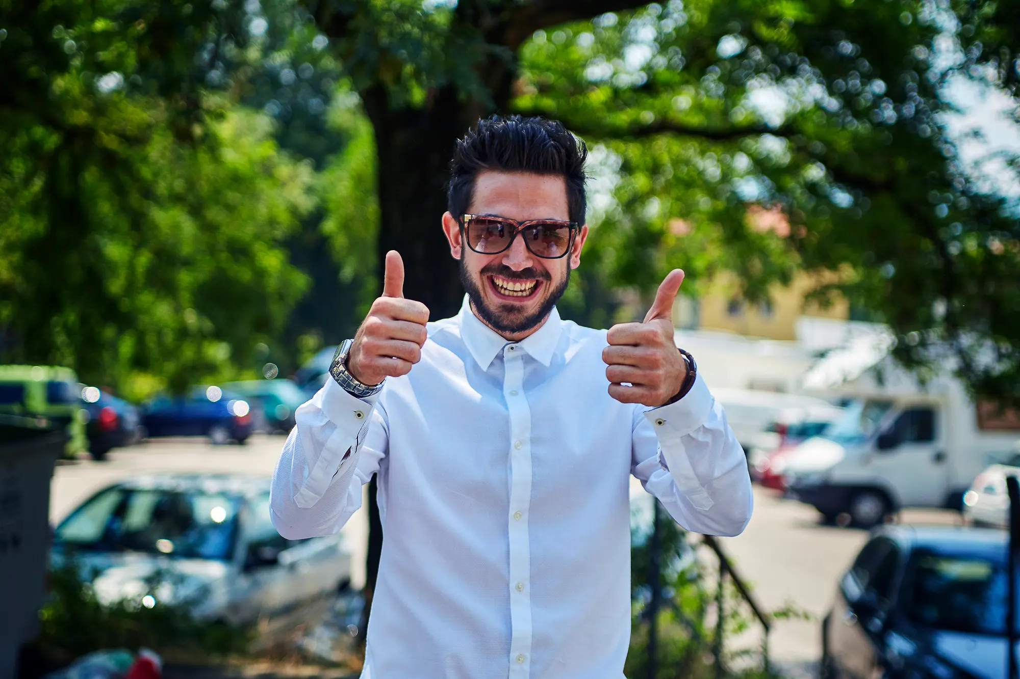 Happy wedding guest in white shirt showing thumbs up gesture during outdoor celebration in Italy
