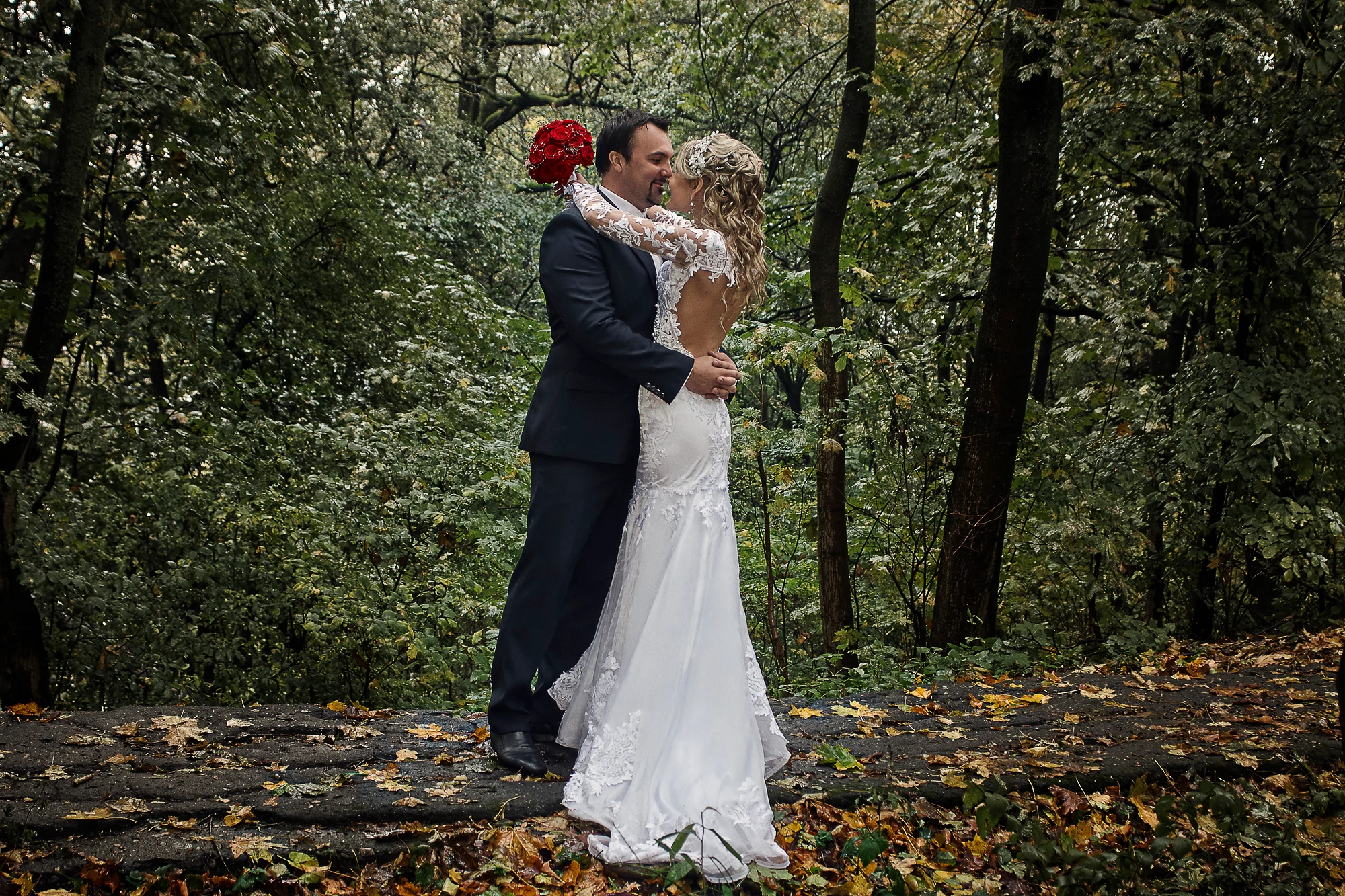 Wedding photographer in Europe capturing bride and groom embracing in green forest park after rain