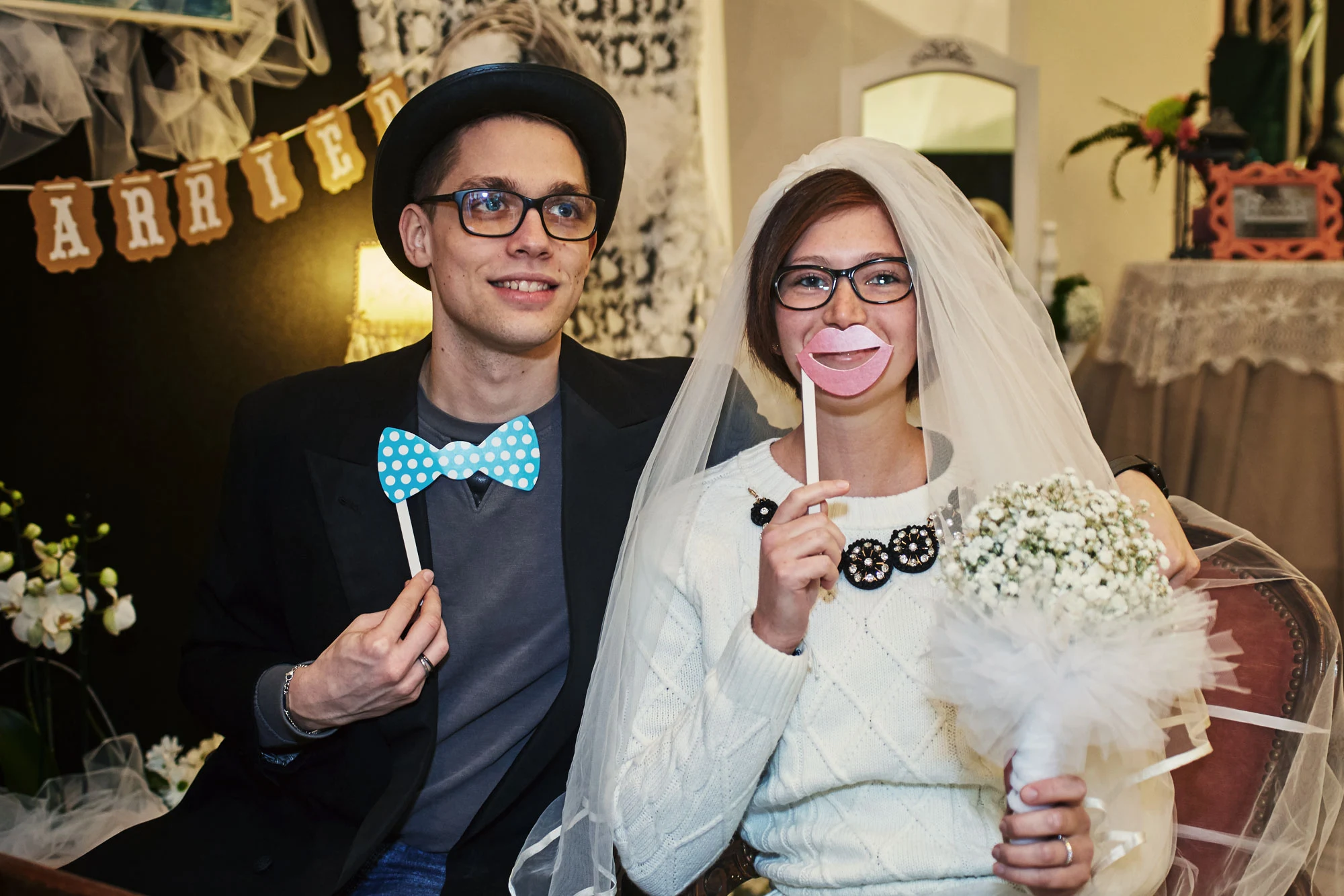 Bride and groom posing in a wedding photobooth with funny paper props and big smiles