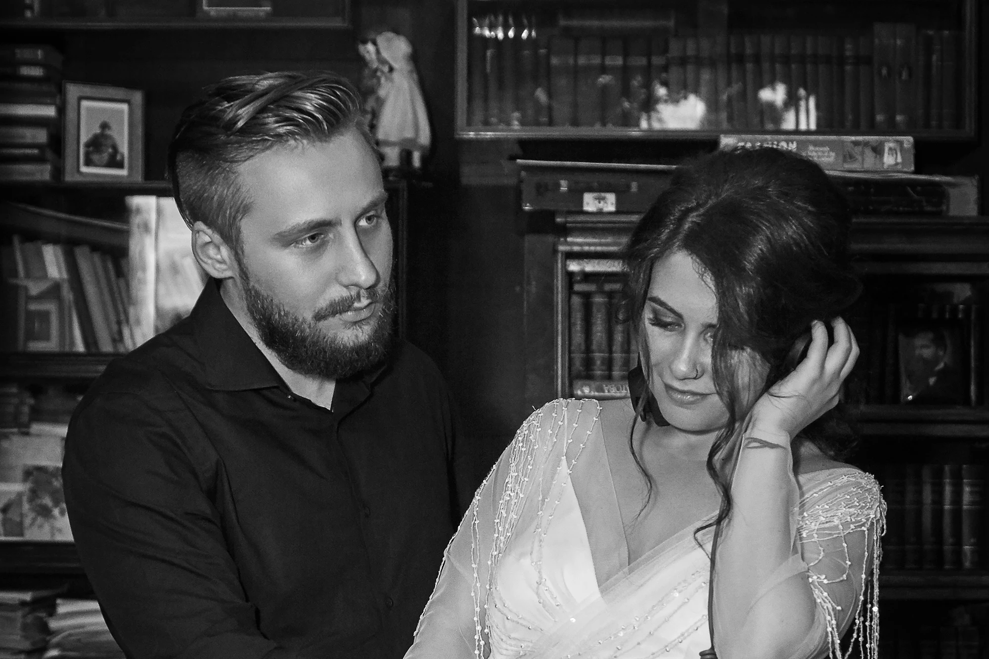 Intimate black and white wedding portrait of a couple sitting together in a cozy room with bookshelves