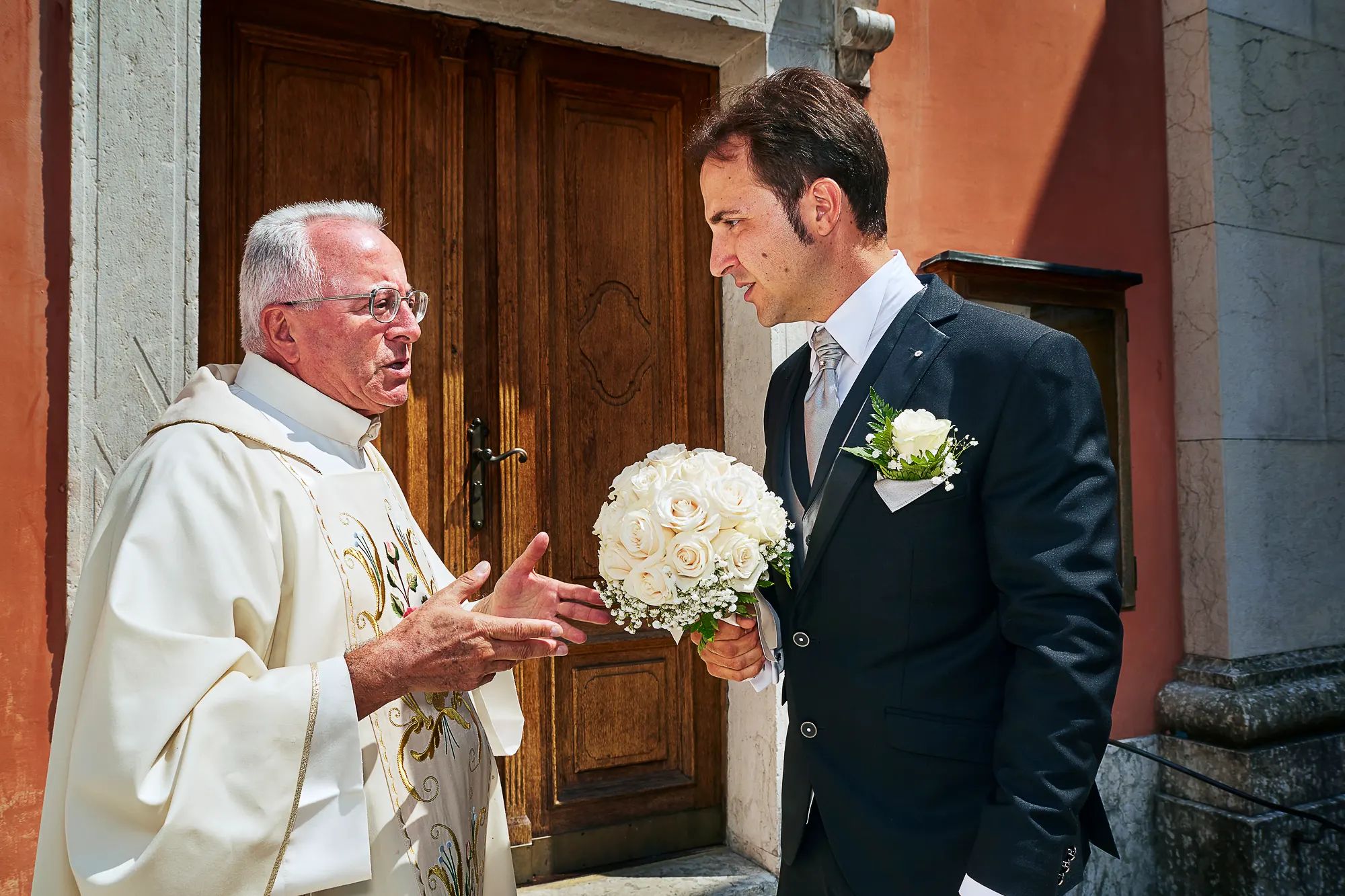 Wedding photographer in Italy photographing priest talking with groom in front of church