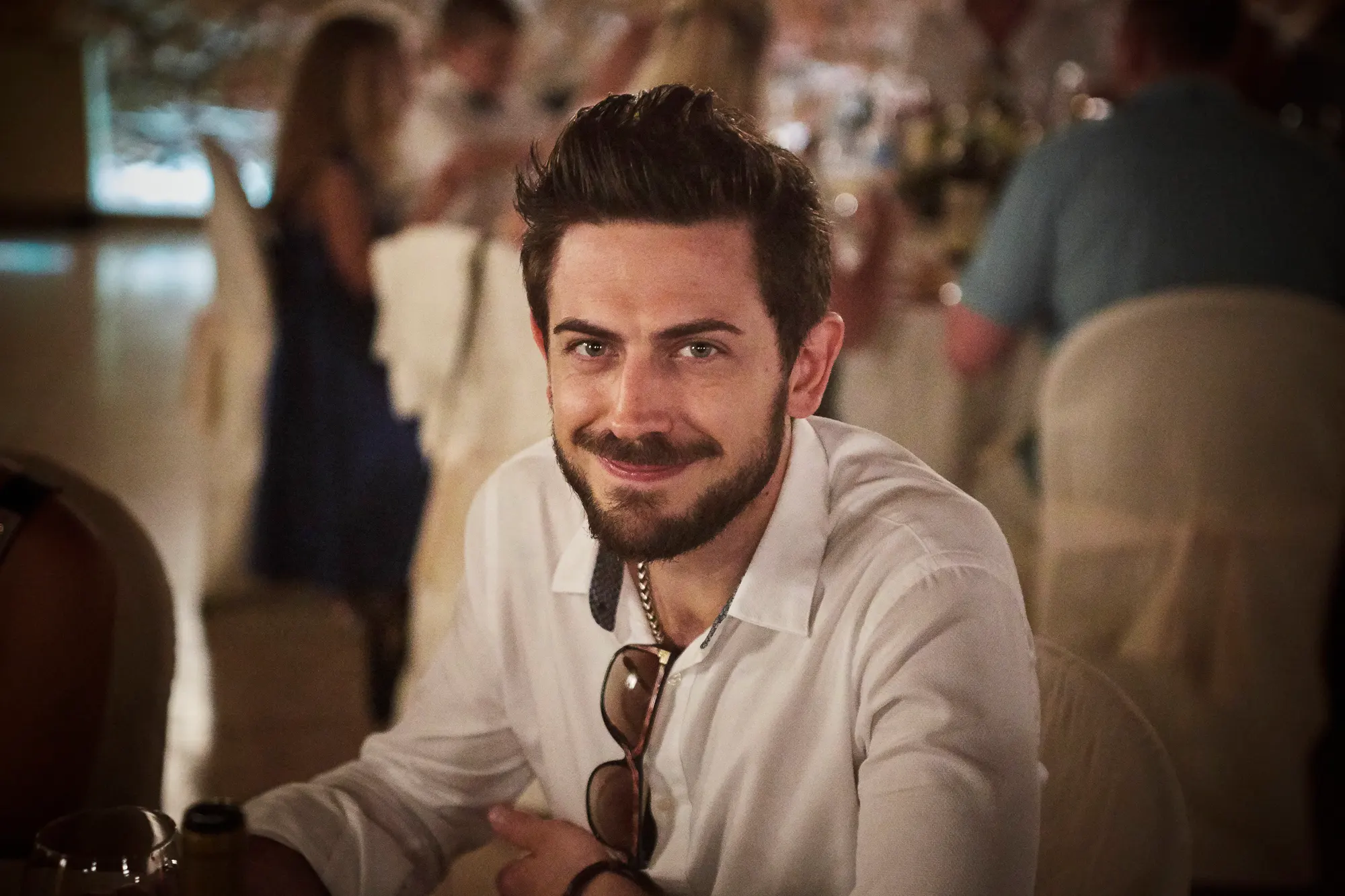 Smiling male wedding guest in a white shirt sitting at the reception table, photographed by a wedding photographer in Italy