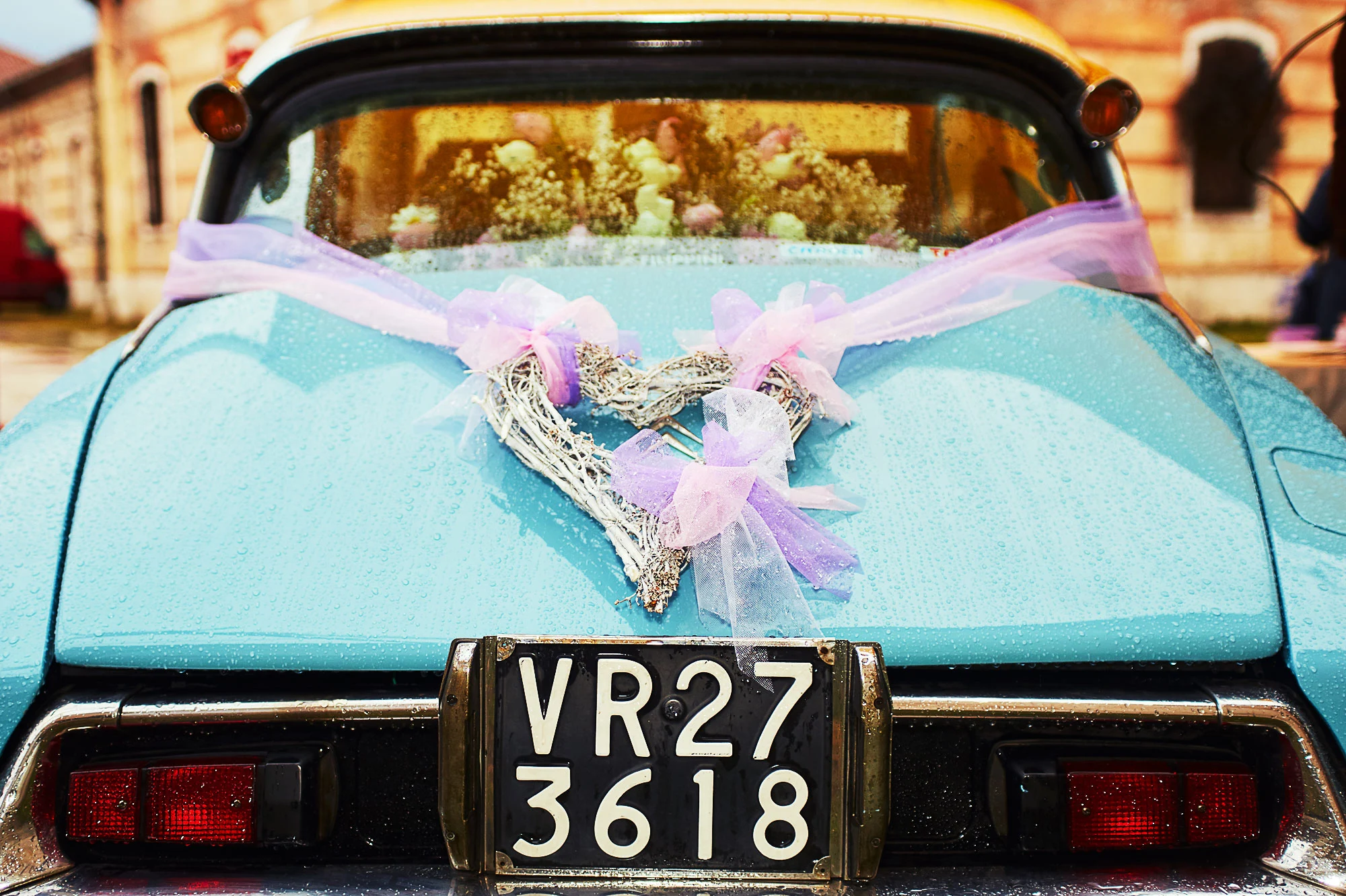 Rear view of a blue vintage wedding car decorated with a heart wreath and pastel ribbons after the rain