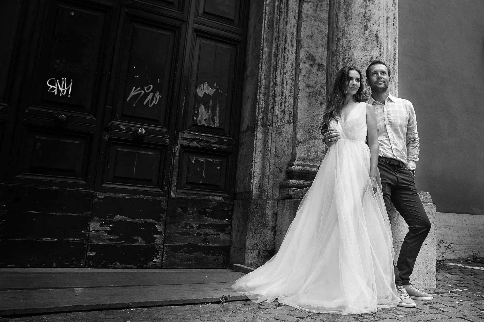 Wedding photographer in Rome Italy capturing couple in wedding dress and casual shirt by old wooden doors